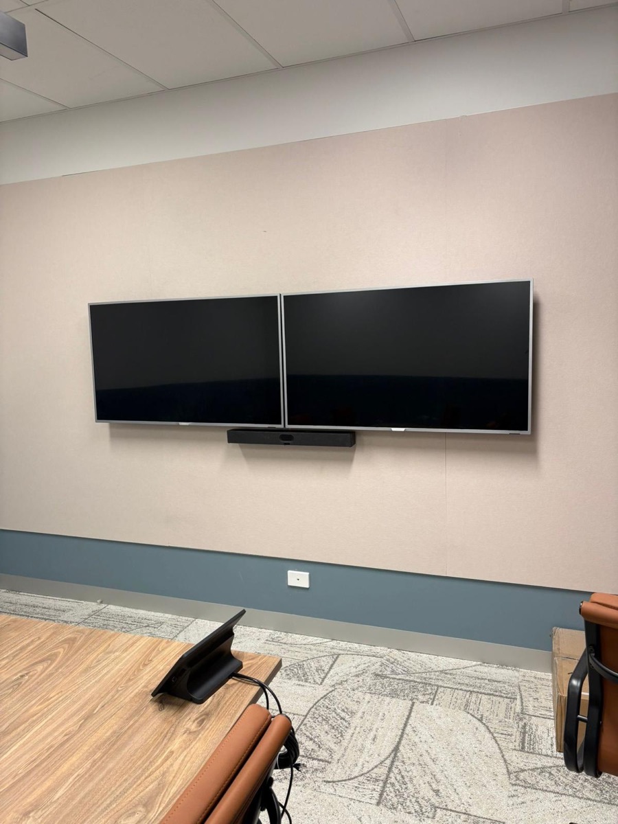 Dual wall-mounted displays with a video conferencing bar in a boardroom